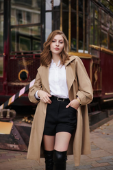 a lady in a white ruffle collared shirt, a pair of black shorts and a trench coat